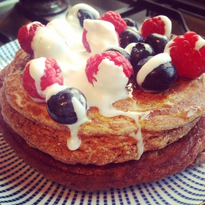 A side view of a stack of Paleo cinnamon pancakes, topped with berries, drizzled with melted raw honey and coconut milk